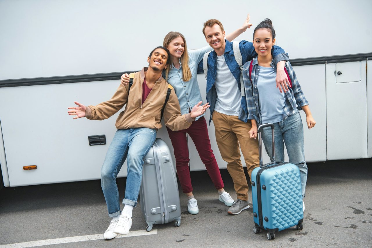 multiethnic happy friends with travels bags gesturing near bus at street
